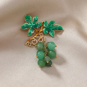 Vintage gold grape brooch with green enamel leaves and beaded grapes on beige fabric