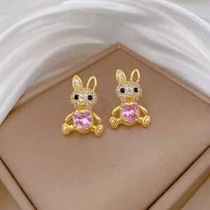 Close-up of golden bunny earrings with pink heart stones and pavé crystals on a silk backdrop