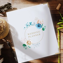 Hochzeitsplaner mit Blumenmuster auf Holztisch mit Schreibwaren und getrockneten Blumen