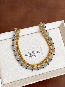 Détail du collier de perles en cristal dorées, bleues et rouges au motif de vagues
