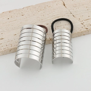 Detail of two silver metal ponytail cuffs with ribbed texture on a stone surface