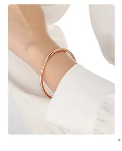 Close-up of a 4mm minimalist rose gold solid bangle on a model's wrist with white fabric