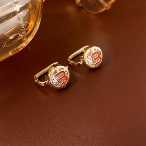 Close-up of golden round earrings with red number 3 and sparkling cubic zirconia stones