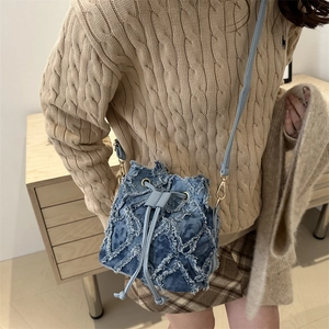 Chic blue denim bucket bag with frayed fringe texture and adjustable shoulder strap