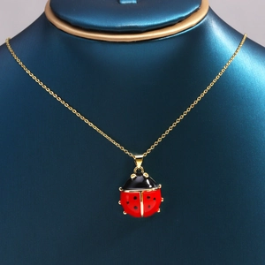 Close-up of a red and black enamel ladybug pendant on a gold necklace on a display