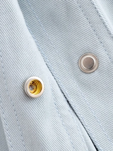 Close-up of light blue twill fabric shirt with silver metal snap button and double stitching