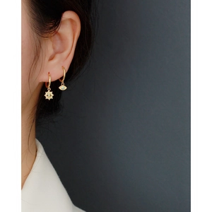 Detail of asymmetric gold evil eye and star earrings with blue zircon on model