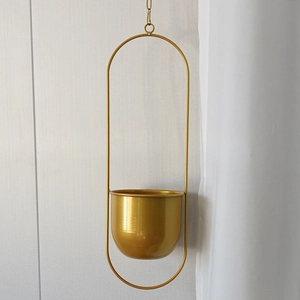 Detail of a golden metal hanging planter featuring a sleek semi-circular pot and oval frame