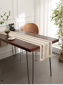 Detail of beige and brown woven table runner with tassels on a dark wood table