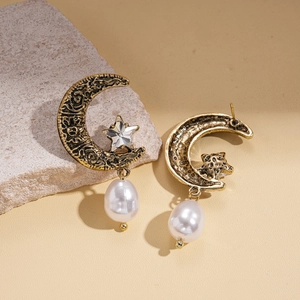 Detail of vintage moon and star earrings with engraved metal texture and pearl drop