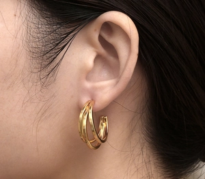 Primo piano di eleganti orecchini a cerchio tripli dorati indossati da una modella