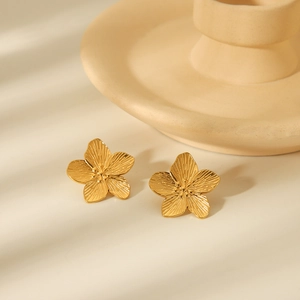 Elegant gold flower earrings in stainless steel on a minimalist decorative dish