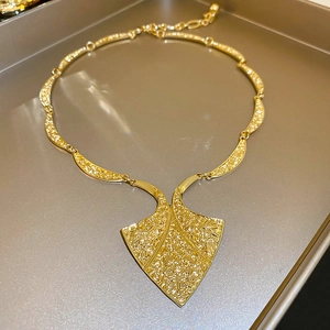 Macro shot of gold geometric necklace with vintage relief pattern on a metallic tray