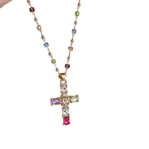 Collier croix dorée avec zircons colorés et chaîne perlée sur fond blanc pur