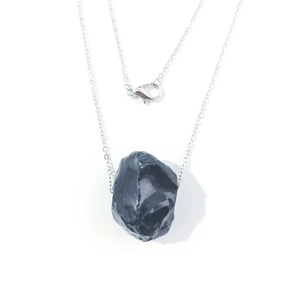 Close-up of raw black natural stone pendant on a silver metal chain with lobster clasp