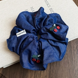Detail of dark blue denim scrunchie with cherry embroidery, pearls, and happiness tag
