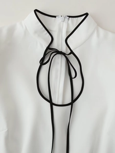 Dettaglio del colletto alla coreana con profili neri e coulisse sul vestito bianco elegante
