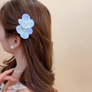 Close-up of light blue fabric flower hair clip with pearls worn by a model
