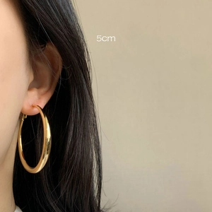 Close-up of a 5cm thick gold hoop earring worn by a model in minimalist style