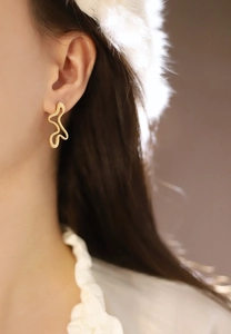 Close-up of golden irregular wavy line earrings with metallic texture on a female model
