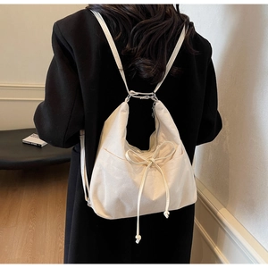 Detail of off-white canvas backpack featuring drawstring closure and decorative bow design
