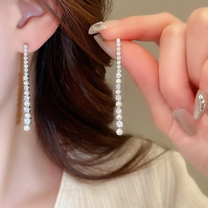 Détail de boucles d'oreilles longues à pampilles avec zircones et perles blanches chic
