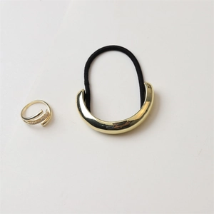 Close-up of golden crescent hair tie and crossover pavé ring on a clean white surface