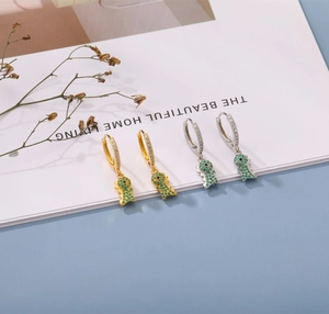 Detail of gold and silver dinosaur hoop earrings with green zircon stones on clean background