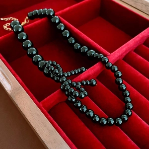 Detail of beaded black bow necklace displayed in a premium red velvet jewelry box