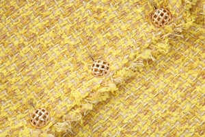 Close-up of yellow tweed fabric texture with decorative gold woven metal buttons