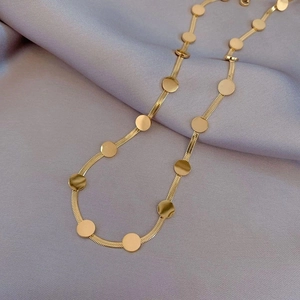 Détail du collier à chaîne serpent dorée avec sequins ronds sur un tissu satiné violet