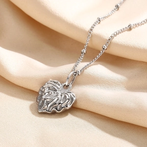 Close-up of heart pendant with wave texture on satellite chain over silk fabric
