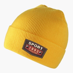 Detailed close-up of bright yellow knit beanie with vintage sport embroidery and rivet