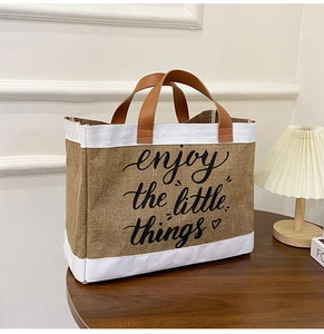 Dettaglio borsa tote in lino con manici in pelle e testo 'enjoy the little things'
