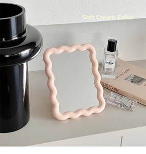 Close-up of cream pink wavy frame mirror on desk with aesthetic decorative setup