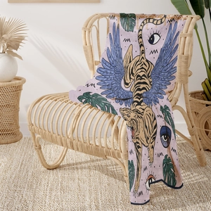 Detail of a soft flannel blanket with tiger and blue wings draped over a rattan chair