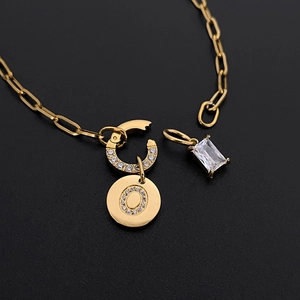 Detail view of gold paperclip chain necklace with crystal letter O and rectangular zircon charm