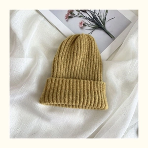 Detailed view of mustard yellow ribbed knit beanie on white linen with dried flowers