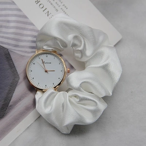 Close-up of white silk scrunchie watch strap with golden case on a magazine