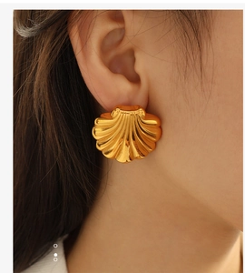 Close-up of golden fan-shaped scallop earrings featuring radiant ribbed texture on model