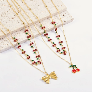 Double-layered gold necklace with red cherry pendants and bow details on stone tray