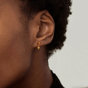 Close-up of minimalist heart-shaped gold earring worn by a model in soft lighting
