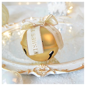 Detail of golden Christmas bell with silk ribbon and Wishes for You print on a tray