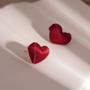 Macro shot of red heart stud earrings with fine brushed fabric texture and gold base