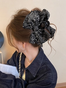 Detail view of the black paisley print bow hair claw clip worn on a woman's long hair