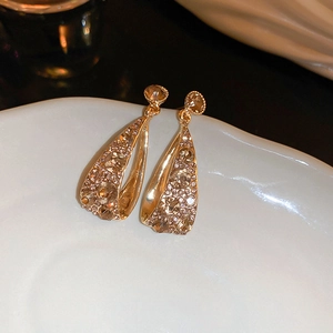 Makroaufnahme goldener Vintage-Ohrringe mit Champagner-Kristallen auf Keramik