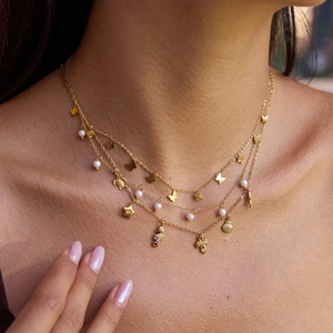 Close-up of layered gold necklace with butterfly and sea animal pendants on model neck