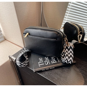 Detail of black PU crossbody bag with golden hardware and wave pattern woven strap