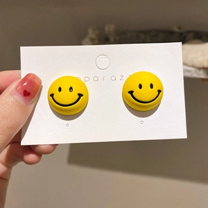 Detailed view of yellow smiley face stud earrings held in hand for size perspective