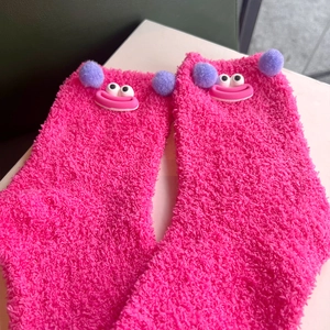 Fuzzy pink coral fleece socks featuring cute big-eyed monster face and purple pom-poms